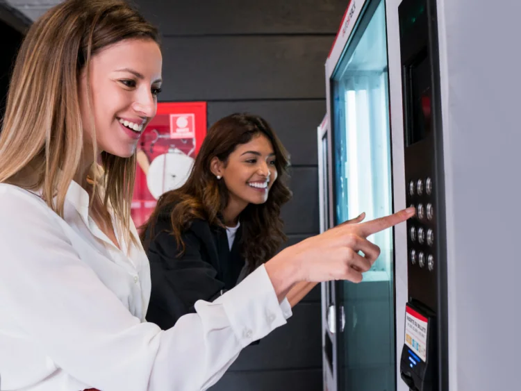 Two women using an industrial vending machine.